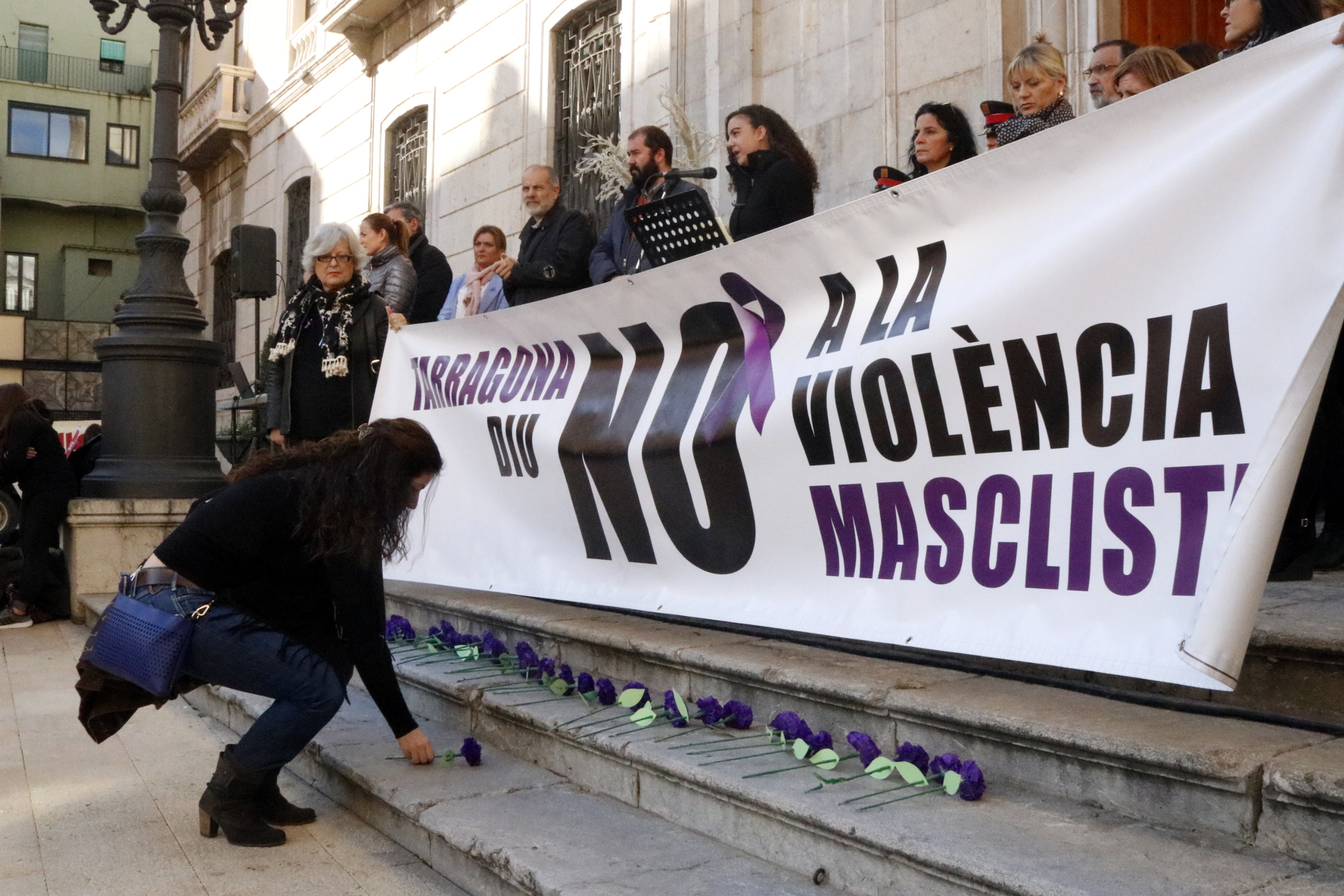 A girl places flower before banner against sexist violence in Tarragona (by ACN)